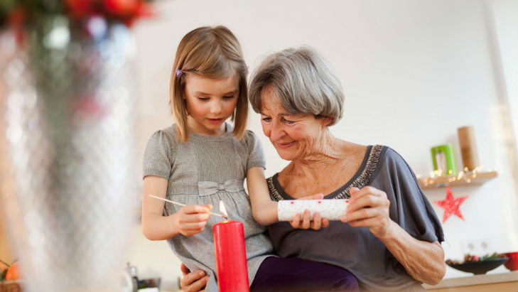 Grandmother helping a granddaughter to light a candle