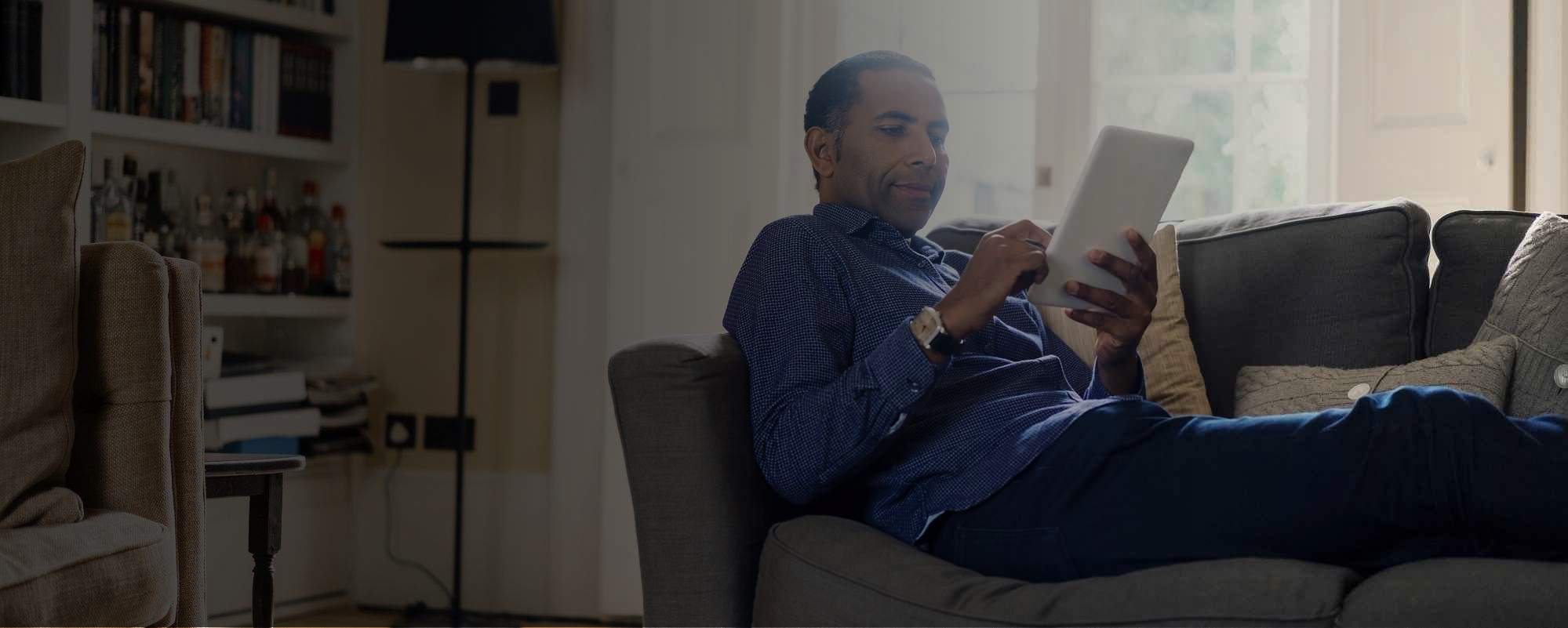 Man relaxing on sofa checking tablet